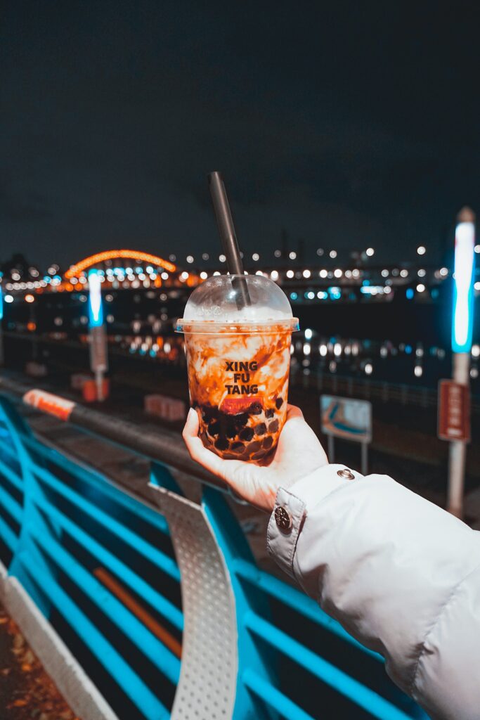 hand holding a cup of bubble tea in front of night scenery