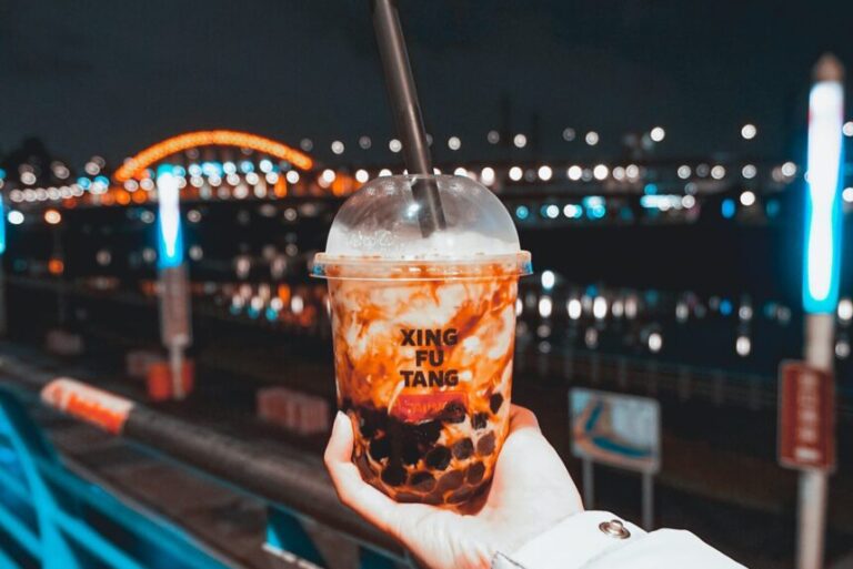 hand holding a cup of bubble tea in front of night scenery